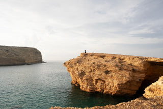 Bild von einer Klippe in Meer, auf der eine Frau steht. 