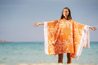 Frau mit orangefarbenem Surfponchon im Meer am Strand